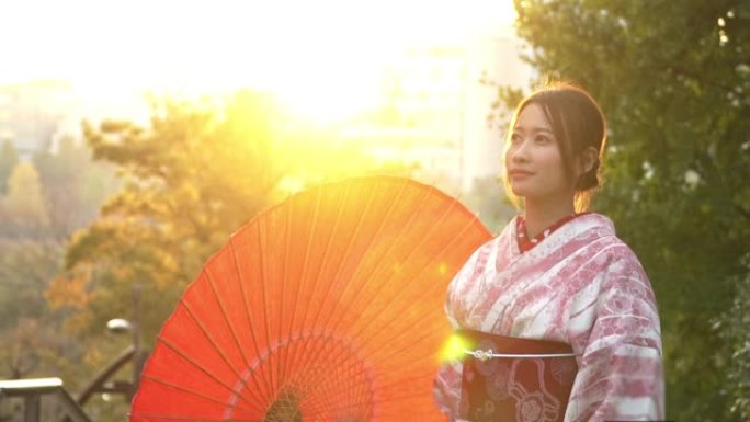 微笑的年轻美丽的亚洲女性游客穿着粉色传统的日本和服连衣裙拿着红色的雨伞在秋天在日本东京市的公园放松和