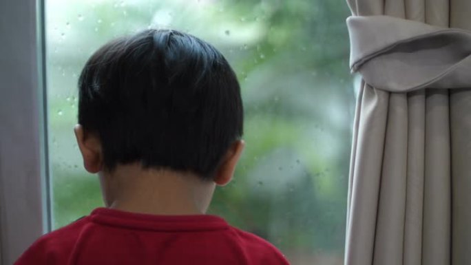 亚洲男婴在窗外看雨和在家学习想象力