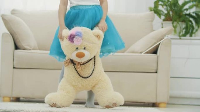 穿着蓝色裙子的短款小女孩站着，手里拿着一只长毛绒的泰迪熊，戴着项链和有趣的头饰。