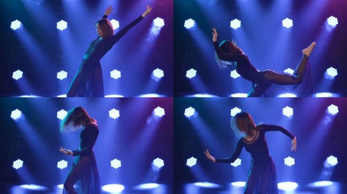 温柔灵活的舞者在蓝色聚光灯前表演当代舞蹈编排的杂技元素。特写。慢动作