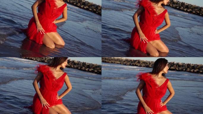 穿着红色连衣裙的性感黑发女人在蓝色海水中跪下摆姿势