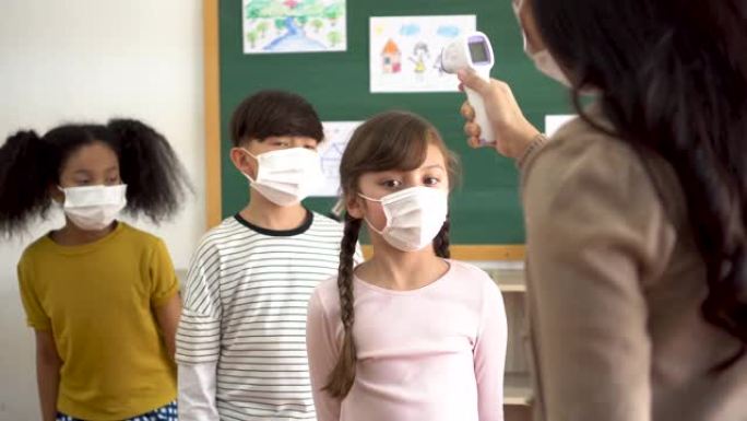 一组学生在教学楼内进行温度检查和扫描。小学生们都戴着口罩，排队进入教室。
