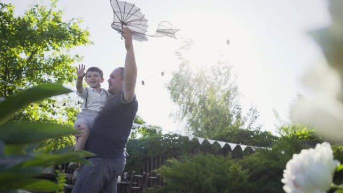 父亲在绿色院子里抱着小儿子玩玩具飞机