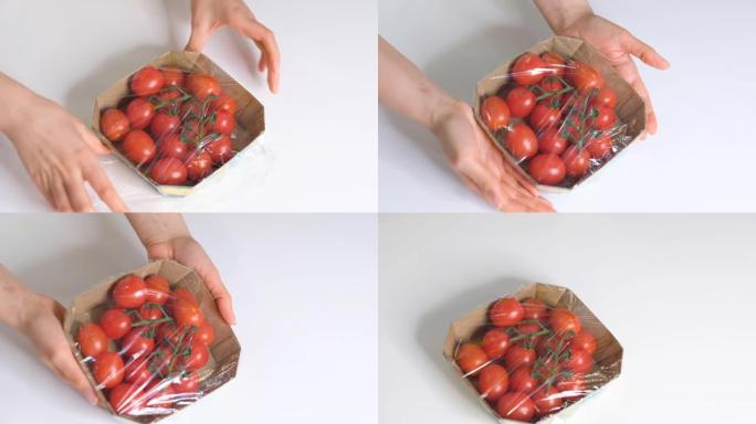女人用食物薄膜在白色桌子上储存食物。包装产品用透明聚乙烯食品薄膜卷。一次性塑料包装的樱桃番茄。慢动作