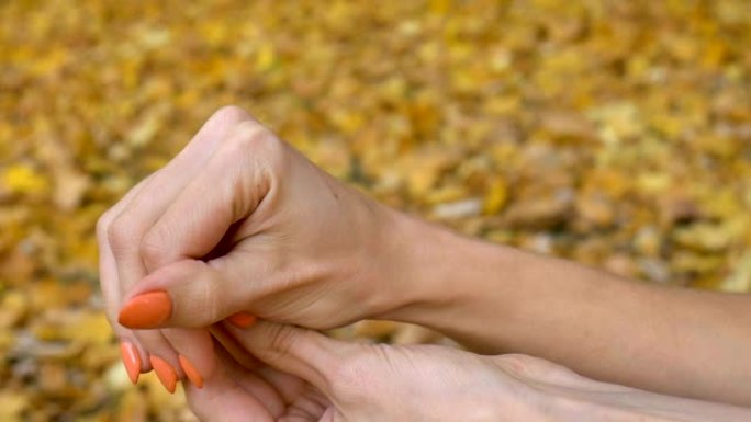橙色修指甲的女性手拿着粉色石英约尼蛋，适合秋季户外黄色落叶背景的vumfit、imbuilding或
