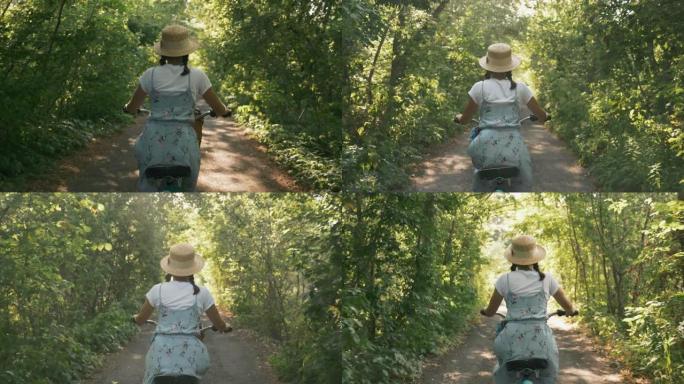 浪漫、梦幻和鼓舞人心的女人穿着飘逸的蓝色太阳裙，在阳光下骑着复古自行车穿过森林路。穿着帽子和衣服的漂