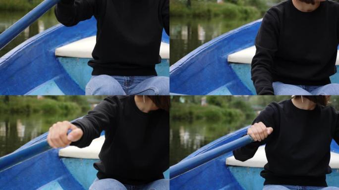 公园湖上女孩划桨船的特写。年轻的高加索女孩划着木船。穿黑色毛衣的女孩在湖上划船。木桨的特写。