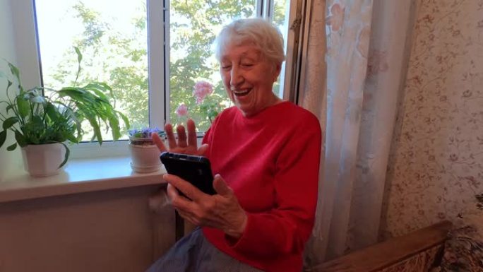 快乐的老年妇女拿着智能手机，在家使用社交媒体看手机屏幕，老年人和技术概念