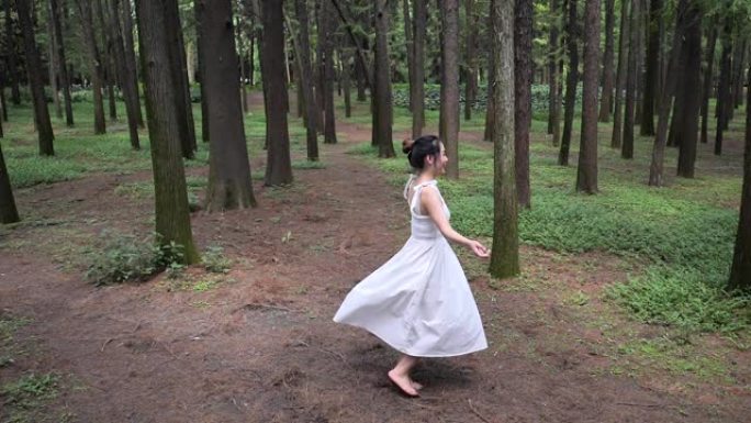 高视角的美丽中国年轻女子穿着白色连衣裙在森林公园跳舞，无忧无虑的女孩快乐旋转，享受大自然中的自我，超
