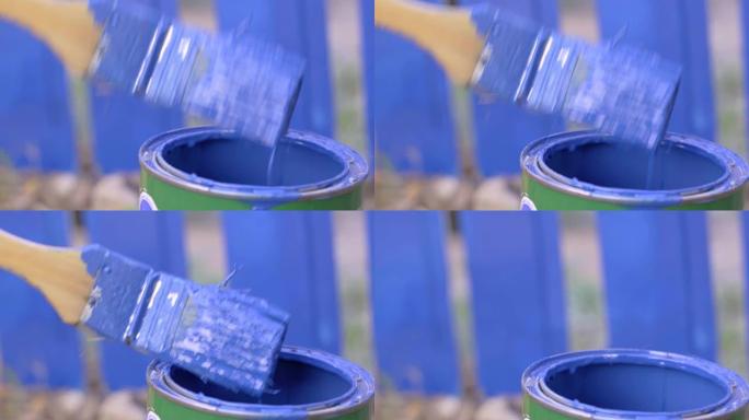 杂工将刷子浸入蓝色染料的金属罐中，并小心地甩掉多余的水滴，以在村庄的建筑工地或土地上油漆围栏或墙壁，