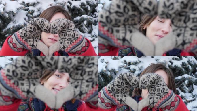 冬天，一个穿着红色外套的年轻高加索迷人女孩的特写肖像直视镜头，摆好姿势，展示了手套手中的一颗大心脏