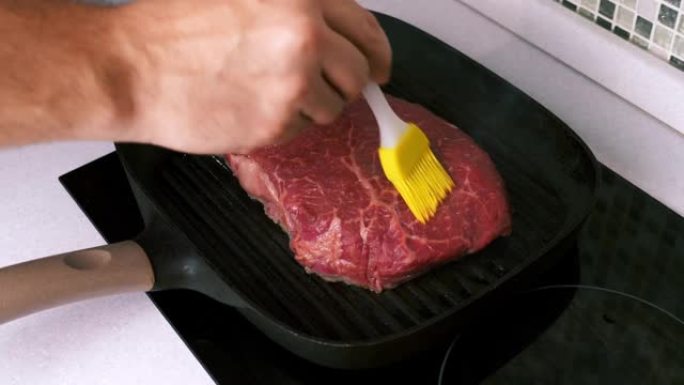 男人用硅胶刷在烤盘上的烤牛排上用手抹油