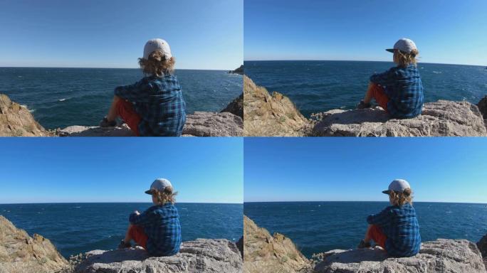 孩子坐在山顶上，看着海浪。