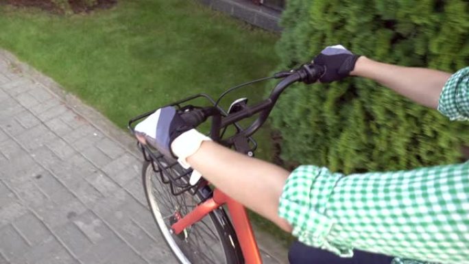 近距离第一人称视角的女性手骑的是橙色城市租赁自行车。女人潮人骑自行车的人把手放在车把上骑自行车，脸不