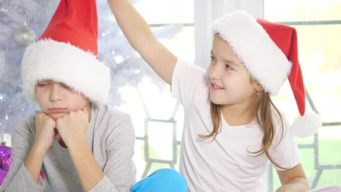 妹妹取笑她生气的哥哥，拉着他的圣诞老人帽子，从一边跳到另一边，微笑着，但心烦意乱的男孩点燃了她。