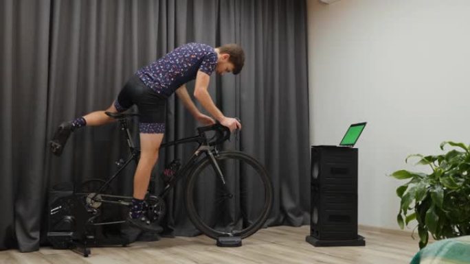 男性开始骑固定自行车教练。男子在室内骑自行车，看着笔记本电脑和自行车电脑的绿色屏幕。减肥概念