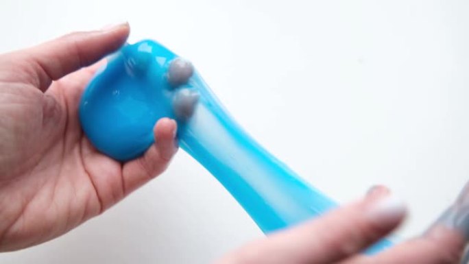 女孩把蓝色粘液伸向两边。玩粘液玩具的女人手。在白色上制作粘液。时髦的液体玩具粘在手上和手指上。4k镜
