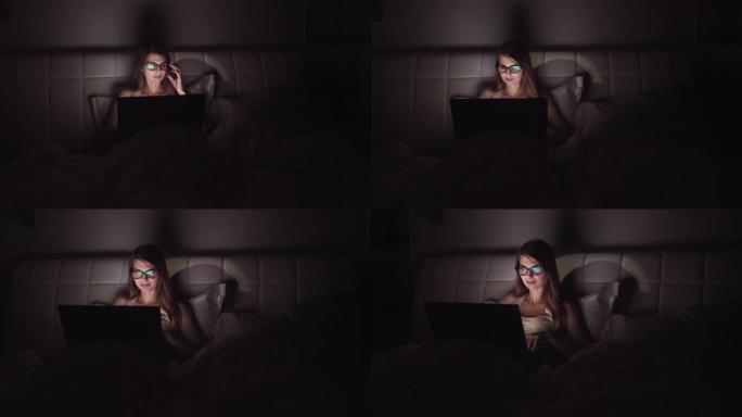 戴眼镜的女人在黑暗中在笔记本电脑上工作。一个女孩在深夜花时间在电脑上的肖像