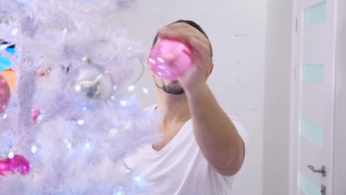 穿着睡衣的人装饰圣诞树，看着粉红色玻璃摆设的倒影。