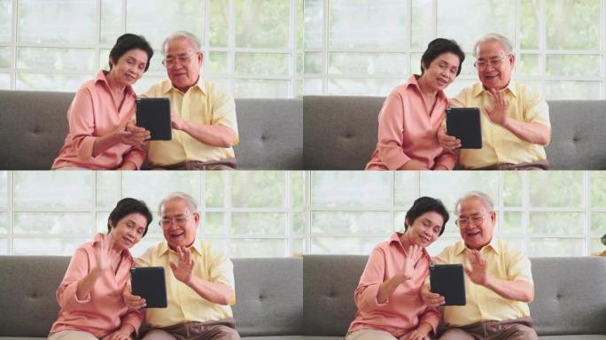亚洲资深夫妇在桌上的视频通话技术中与家人挥手大笑。