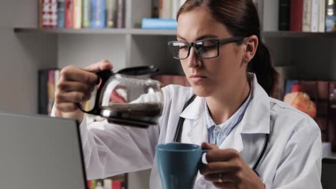 医生倒咖啡。办公室工作场所穿着白大褂的女医生在电脑上工作时，将咖啡机中的咖啡倒入蓝色杯子和饮料中