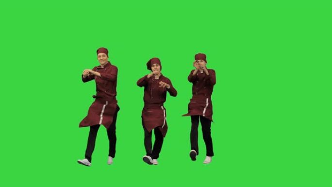 三位微笑的厨师穿着红色制服同步在绿色背景下跳舞，并在绿色屏幕上指向相机，色度键