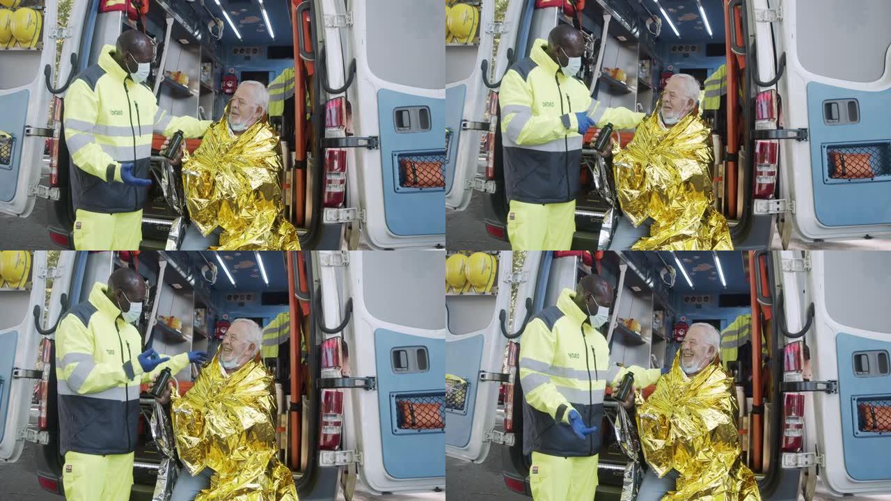 一名护理人员的慢动作视频，他正在用金色的保暖毯帮助坐在救护车上的成熟男人