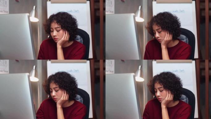 迷人的年轻亚洲女商人正在坐在办公桌前的台式计算机上工作，对工作感到疲惫和无聊。懒散女工过度劳累感觉工