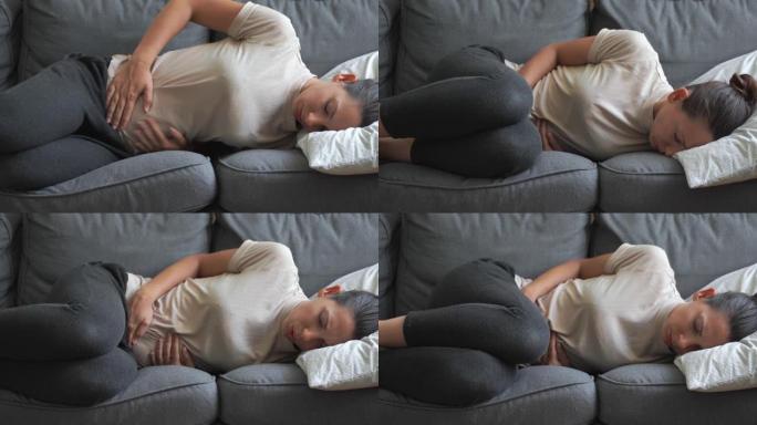 腹部疼痛的女人躺在灰色沙发上。痛苦的时期。消化系统问题。