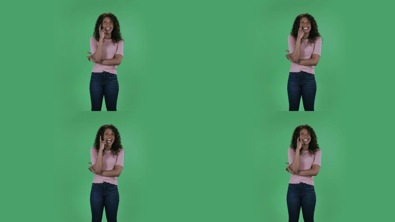 美丽的非洲裔美国年轻女子的肖像正在做白日梦，微笑着抬头。在工作室的绿色屏幕上燃烧着黑发，波浪状的牛仔