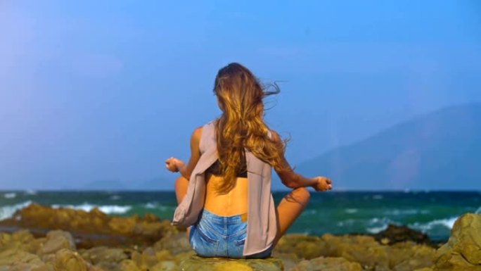 女孩坐在海风的荷花姿势摇动头发后视图