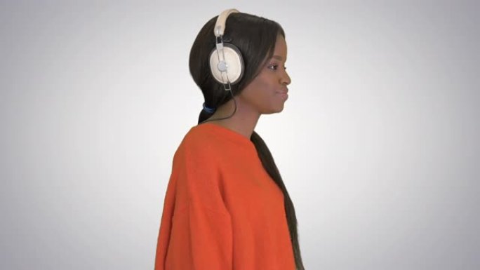 带着耳机微笑的非洲裔美国妇女走路听渐变背景上的音乐