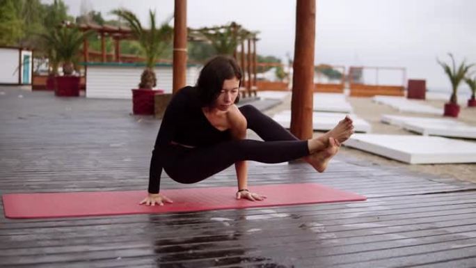 黑衣女孩在沙滩上的木地板上做瑜伽，女孩在双手上进行瑜伽元素平衡体重