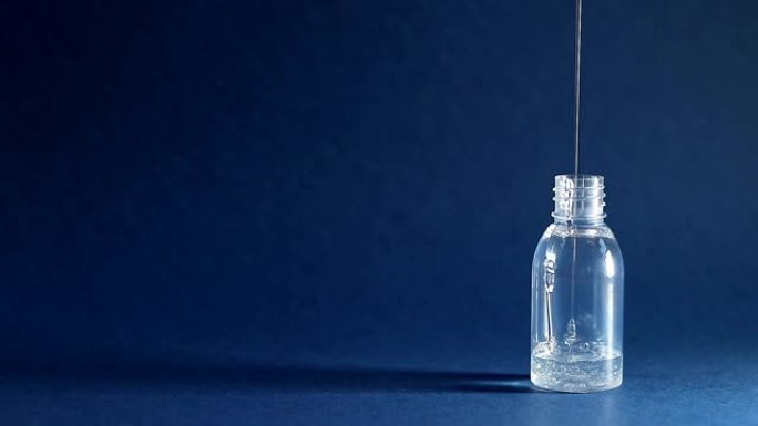 浓透明液体倒入深蓝色背景的空塑料容器中。化妆品 (凝胶或洗发水) 填充旅行瓶