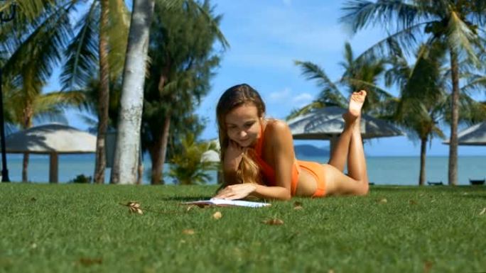 穿着泳衣的好女孩在棕榈树间的草地上读书