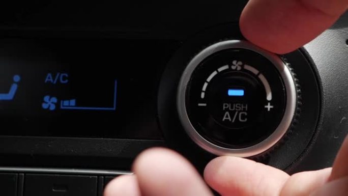 按下按钮打开汽车空调的特写镜头。男人的手转动按钮，调节车内的舒适性