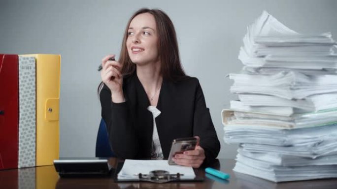 穿着黑色办公室制服的沉思女商人坐在成堆的文书工作，艰难的财务计算和加班工作日之间。微笑经理使用智能手