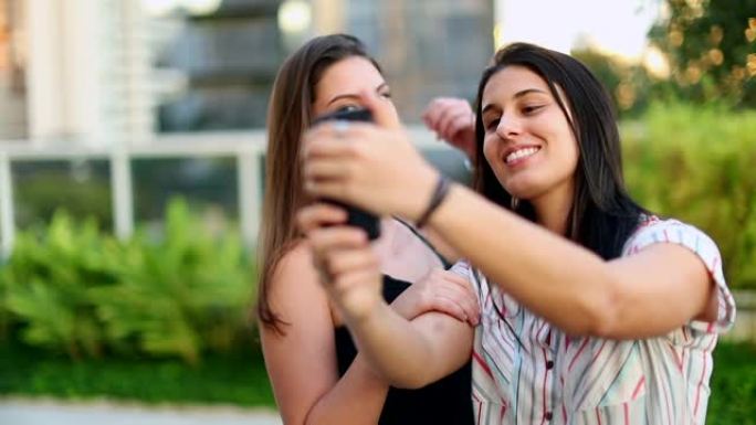 两个年轻女人在外面自拍。拿着智能手机拍照的千禧女孩