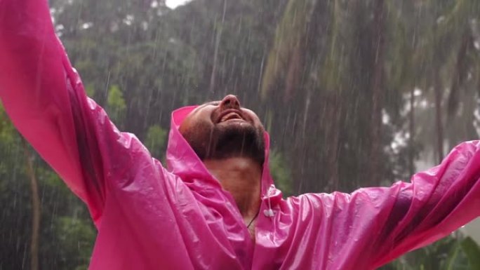 一个穿着粉红色雨衣的成年男子享受热带雨。慢动作