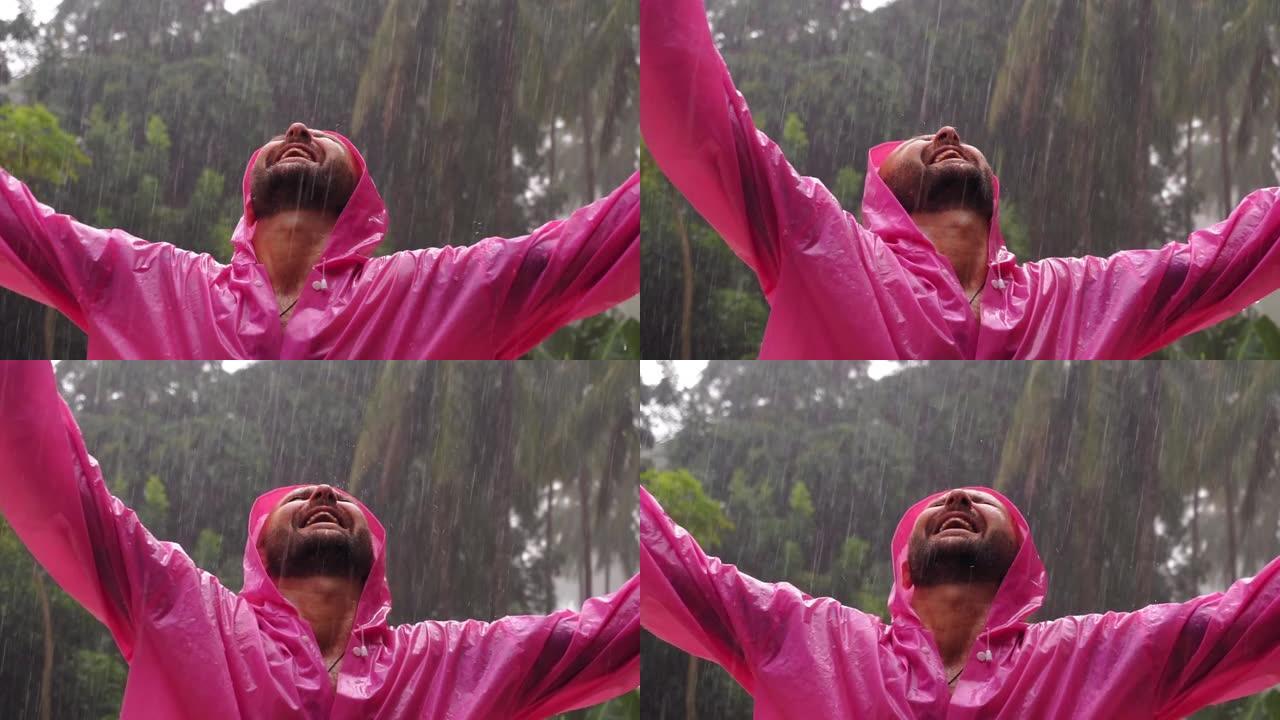 一个穿着粉红色雨衣的成年男子享受热带雨。慢动作