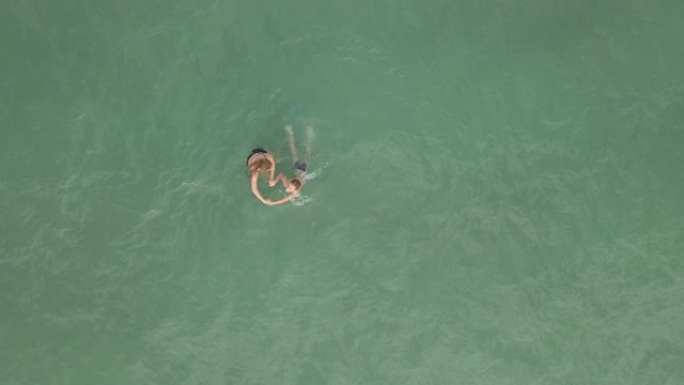 空中慢动作镜头。在蓝色的大海中玩耍的母子自上而下的视图