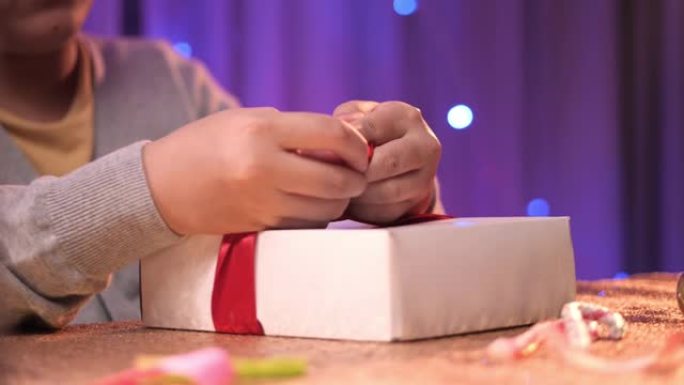 亚洲男孩将红色蝴蝶结绑在礼品盒上，准备圣诞派对。