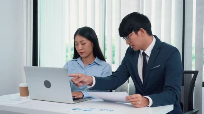 亚洲男经理在他们的办公桌上教员工簿记。