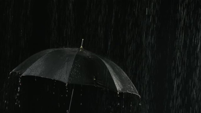 雨中敞开的黑色雨伞，水流通过它向下流动。在黑暗的背光摄影棚中近距离拍摄。慢动作