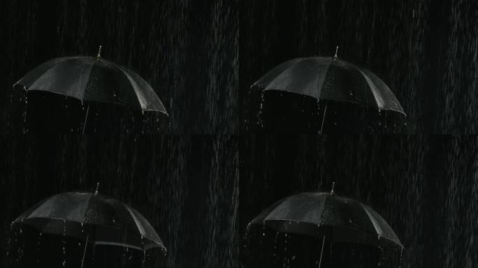 雨中敞开的黑色雨伞，水流通过它向下流动。在黑暗的背光摄影棚中近距离拍摄。慢动作