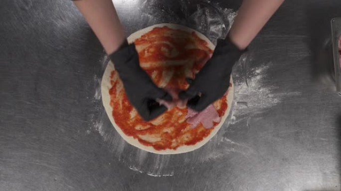 在餐馆准备意大利披萨。厨师的俯视图将培根和酱汁放在面团上