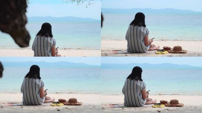 亚洲妇女在暑假时间坐在海滩上写明年的新年决议