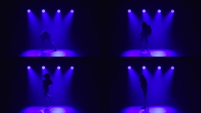 一个波浪形头发的女孩专业跳舞爵士乐放克元素。在上方蓝色灯光的背景下，在黑暗的工作室中舞者的剪影。慢动