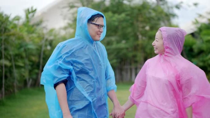 亚洲夫妇穿着五颜六色的雨衣微笑着，在大自然的雨中玩耍很开心
