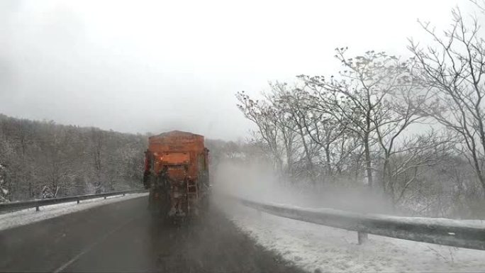 扫雪机服务卡车和铲运机在路面上撒盐的背面视图，以防止在暴风雨的冬天里结冰，慢动作